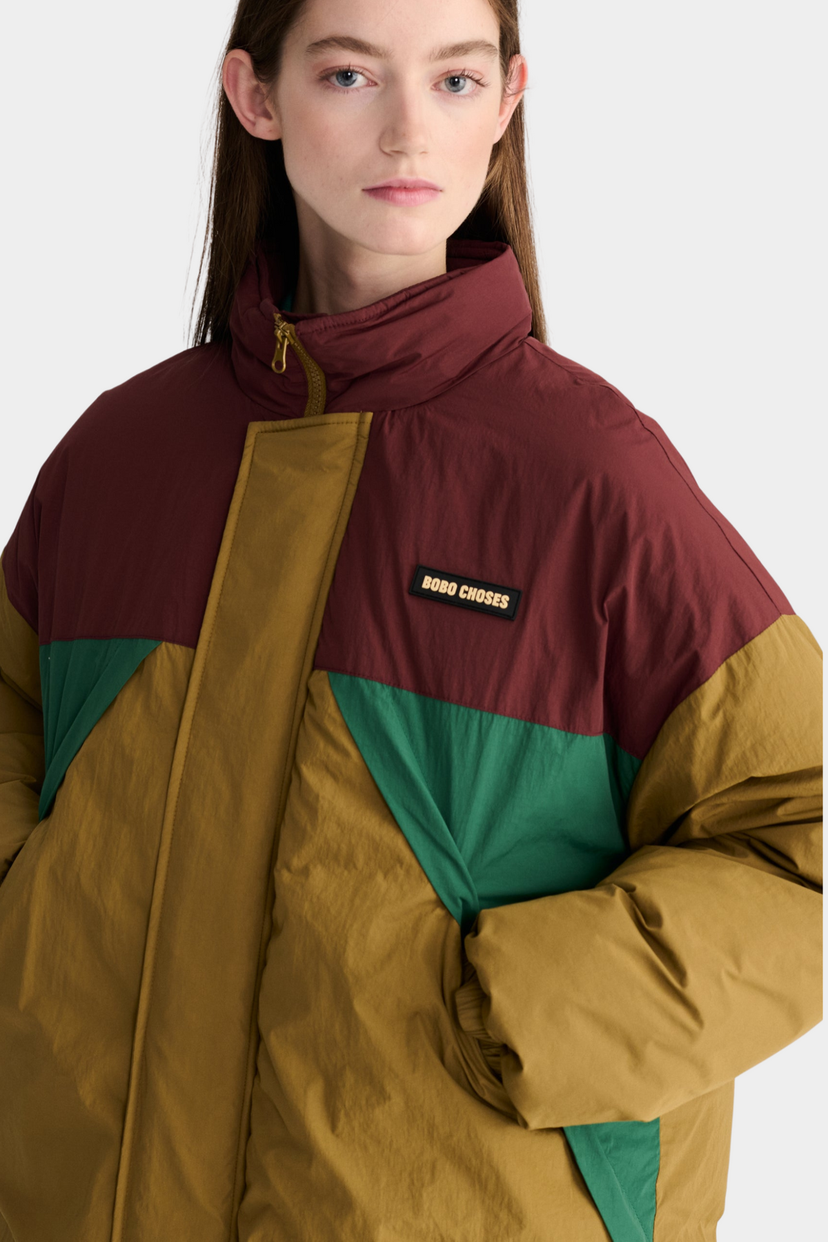 Detalle de la parka acolchada Bobo Choses con bloques de color mostaza, burdeos y verde y cuello alto