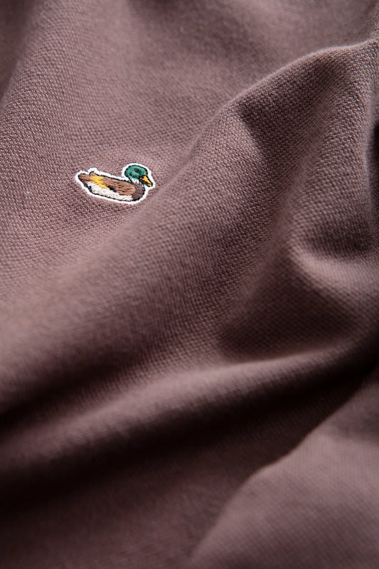 Detalle del polo marrón chocolate Edmmond Studios con cuello de botones y pequeño pato bordado en el pecho
